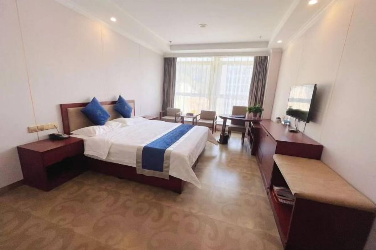Ein Hotelzimmer mit Bett, Nachttischen, Schreibtisch, Stuhl, Fernseher und einem Fenster mit Vorhängen.