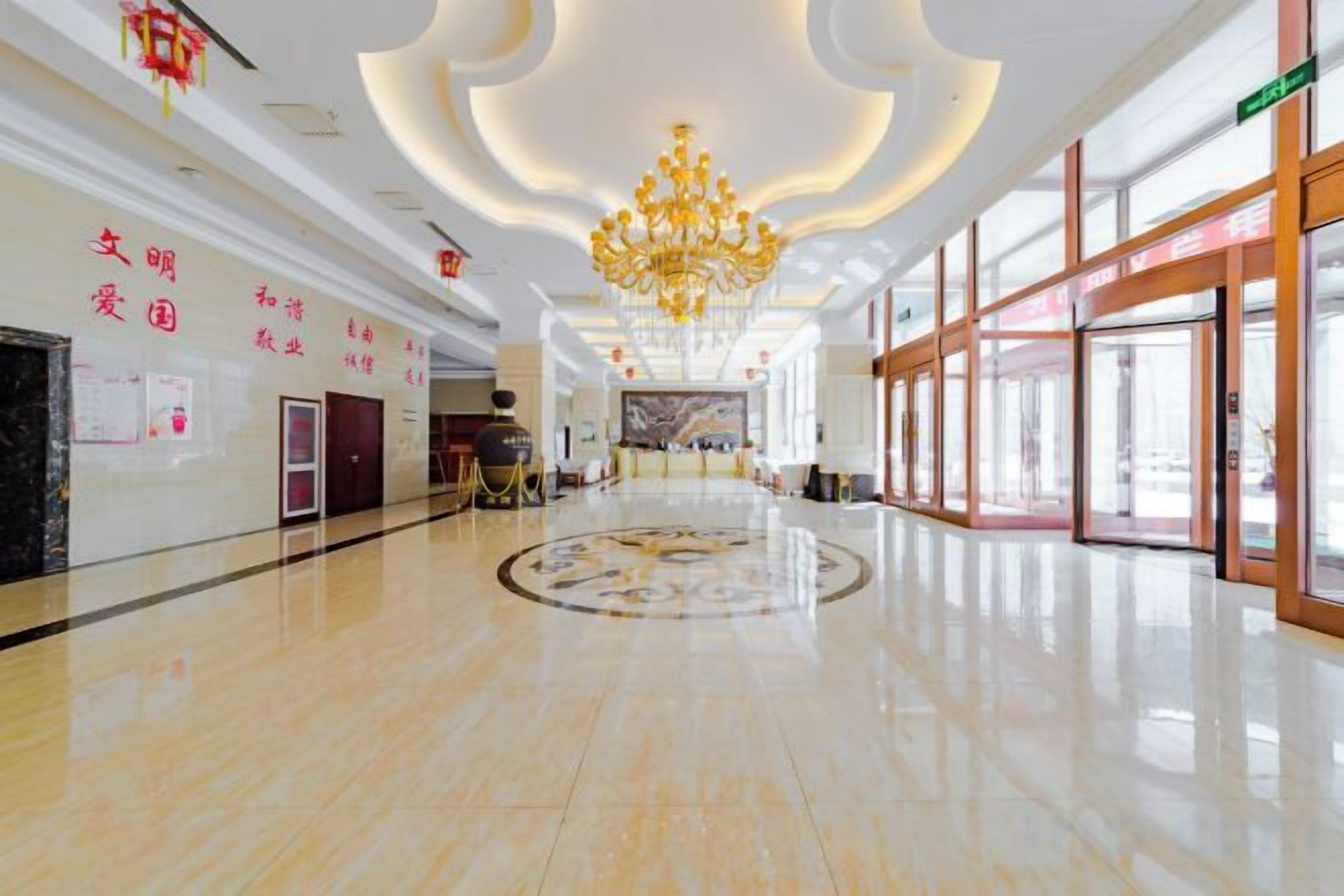 A spacious hotel lobby with a polished floor, a grand chandelier, and a large circular decorative element in the center.