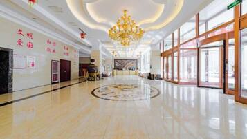 A spacious hotel lobby with a polished floor, a grand chandelier, and a large circular decorative element in the center.