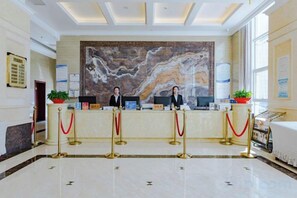 Un área de recepción con suelo de mármol, dos recepcionistas, una gran pared de mármol y un mostrador de recepción.