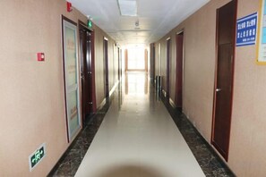 Un pasillo largo y estrecho con puertas a ambos lados, una fuente de luz al final y un cartel en la pared derecha.