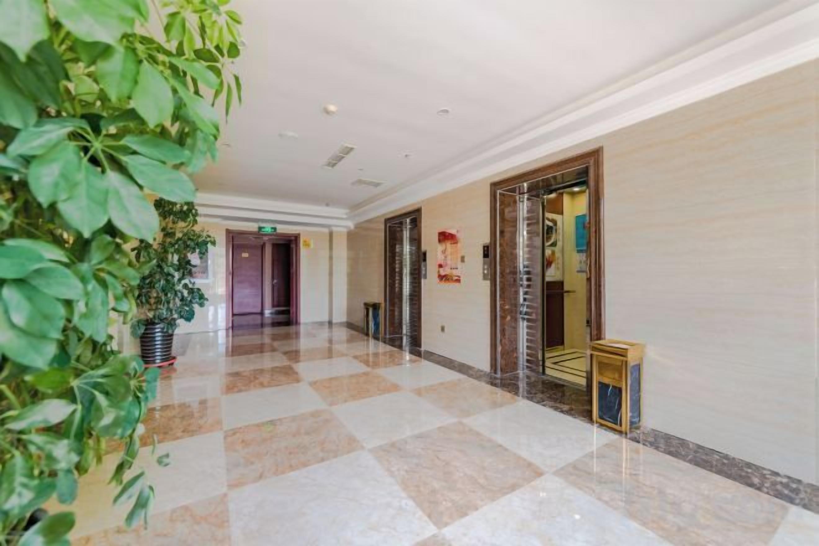 Un pasillo de hotel con piso a cuadros, una planta en maceta y una puerta con un cartel.
