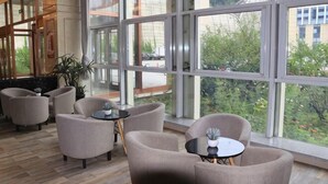 Un vestíbulo amplio con ventanas grandes, asientos cómodos y vistas al exterior con zonas verdes.