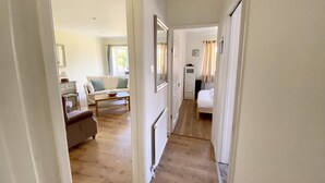 A narrow hallway with wooden flooring leading to a living area with a sofa, a coffee table, and a chair. - Daisy Cottage by NewFo rest (Lymington)