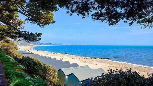 A coastal view with a beach, clear sky, and a row of beach huts. - Daisy Cottage by NewFo rest (Lymington)