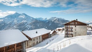 A snow-covered mountain village with stone buildings and wooden structures, featuring a prominent stone building with balconies.