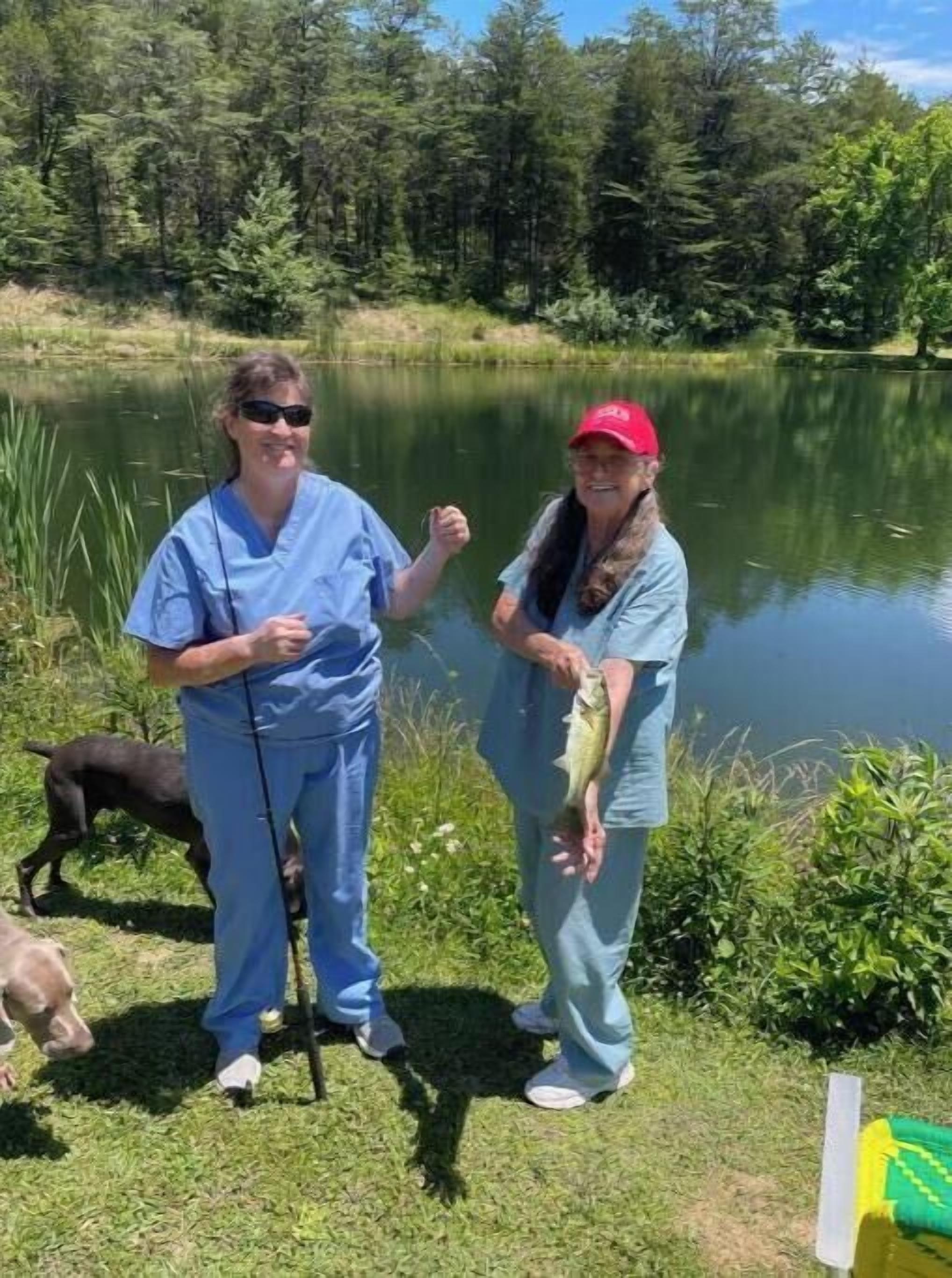 Two people standing by a lake, one holding a fish.