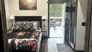 Une chambre à coucher avec un lit, deux lampes de chevet, un tableau au mur et une vue sur un patio extérieur avec une table et des chaises.