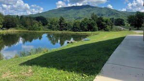 Une vue paisible sur un lac, avec une montagne en arrière-plan, une zone herbeuse et un chemin en béton.