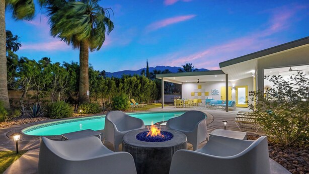 Ein moderner Poolbereich im Freien mit Feuerstelle, Liegestühlen und einer überdachten Terrasse mit Sitzgelegenheit und Tisch.