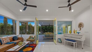 Ein modernes Wohnzimmer mit Klavier, einer Couch, einem Couchtisch und einem großen Fenster mit Blick auf einen Garten.