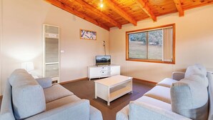 Ein Wohnzimmer mit Holzbalkendecke, einer weißen Unterhaltungseinheit, einem großen Fenster und grauen Sofas.