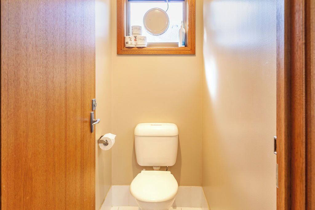 A small, clean bathroom with a toilet, a roll of toilet paper, and a mirror above the toilet.
