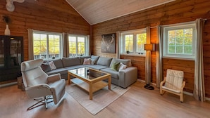 A log cabin interior with a sectional sofa, a glass coffee table, a modern armchair, a floor lamp, and a fireplace.