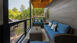 Eine überdachte Veranda mit einem blauen Sofa und Korbstühlen, mit Blick auf einen bewaldeten Bereich.