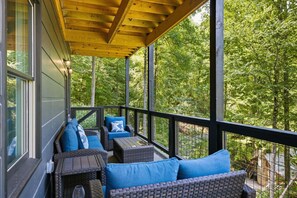 A covered outdoor seating area with wicker furniture and blue cushions, overlooking a forested area.