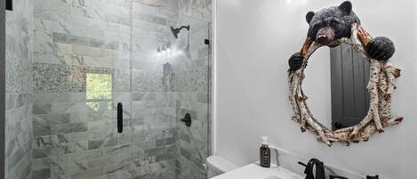Un baño moderno con ducha de vidrio, un lavabo blanco y un espejo con motivos de oso.