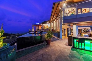 Un moderno espacio al aire libre con bar, piscina, taburetes y zona de estar.