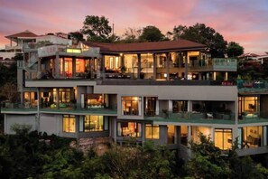 A multi-story building with balconies and large windows, surrounded by greenery. - Villa Skyfall : Spectacular 8 Bedroom Pool Villa with Private Cinema (Koh Samui)