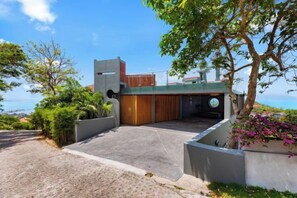 Una casa moderna con entrada pavimentada, un portón de madera y vista al mar.