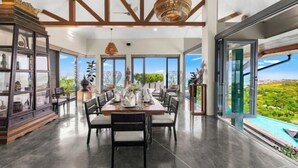 A spacious dining area with a long table, chairs, and a view of a lush landscape through large windows. - Villa Skyfall : Spectacular 8 Bedroom Pool Villa with Private Cinema (Koh Samui)