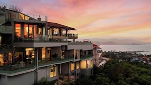 A multi-story hotel with balconies and large windows, overlooking a body of water and mountains. - Villa Skyfall : Spectacular 8 Bedroom Pool Villa with Private Cinema (Koh Samui)
