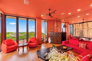 A modern living room with a large window, red furniture, and a ceiling fan. - Villa Skyfall : Spectacular 8 Bedroom Pool Villa with Private Cinema (Koh Samui)