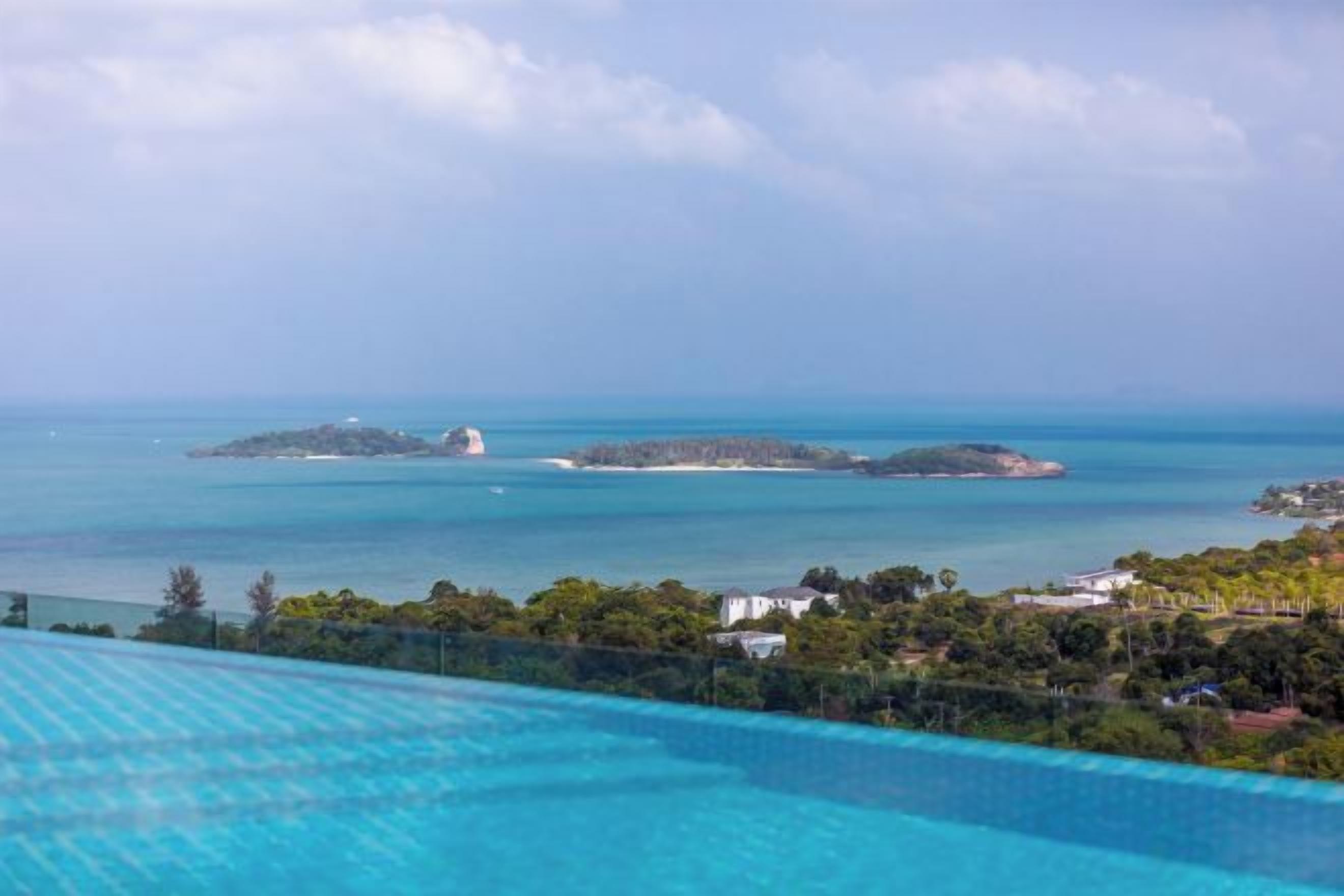 A pool with clear blue water, surrounded by greenery and overlooking a calm sea with distant islands.
