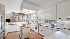 Une cuisine moderne avec des meubles blancs, un îlot central, un four encastré et un four à micro-ondes.