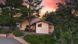 Une maison à deux étages, dotée d’un toit en pente, entourée d’arbres denses et accessible par une allée en gravier.
