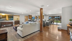 A spacious living area with a sofa, wooden flooring, a dining table, and a kitchen in the background.