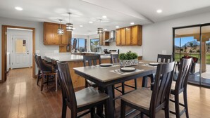 A modern kitchen with wooden cabinets, a central island, and a dining area with chairs and a table.