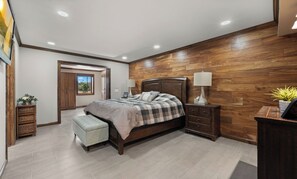 A bedroom with a wooden headboard, a bed with a checkered bedspread, a bedside table with a lamp, a nightstand, and a small bench.