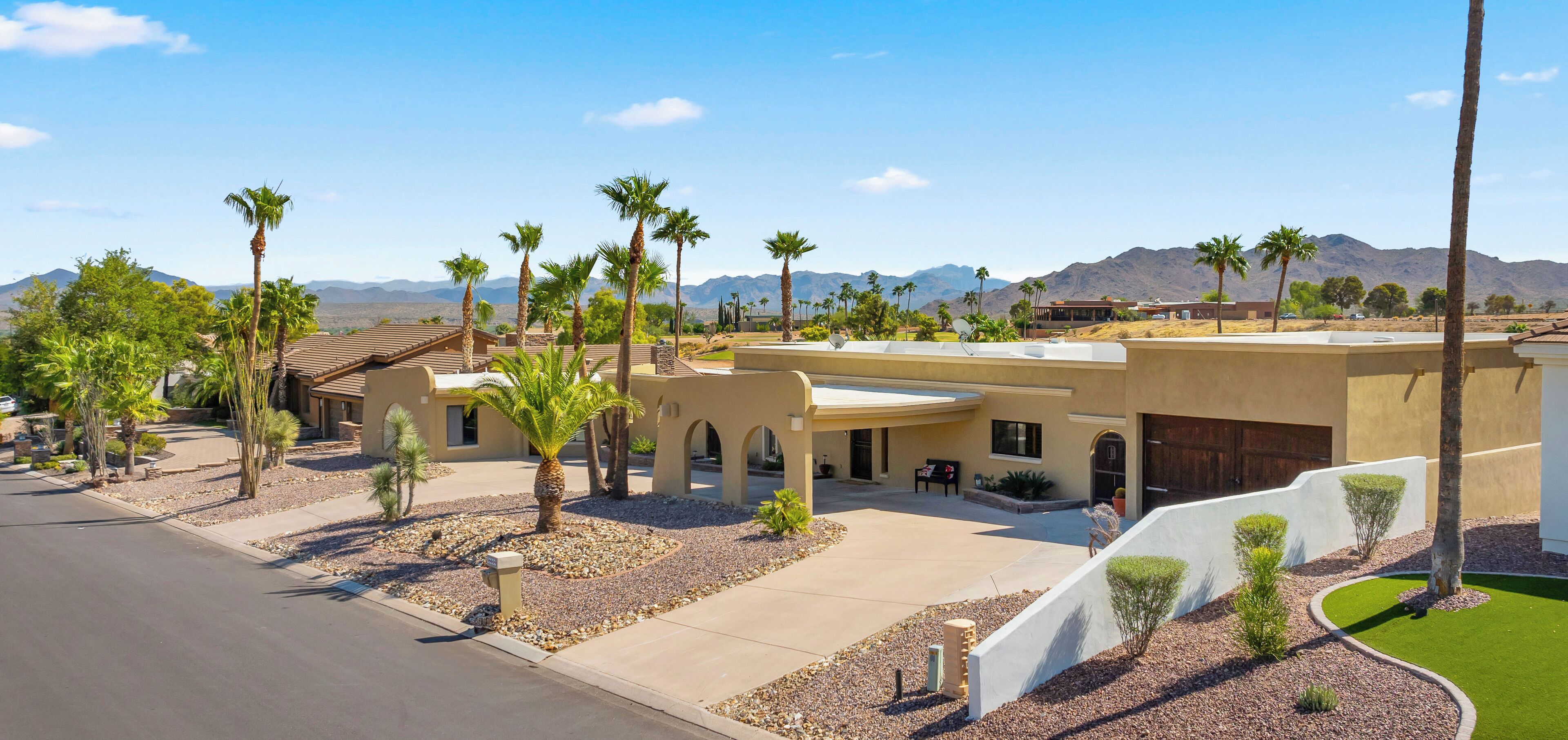 A modern building with a curved roof, surrounded by palm trees and a clear view of mountains in the background.