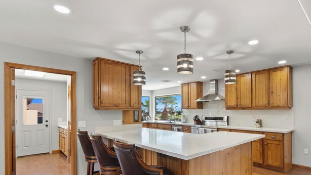 A modern kitchen with wooden cabinets, a large island, bar stools, and pendant lighting.