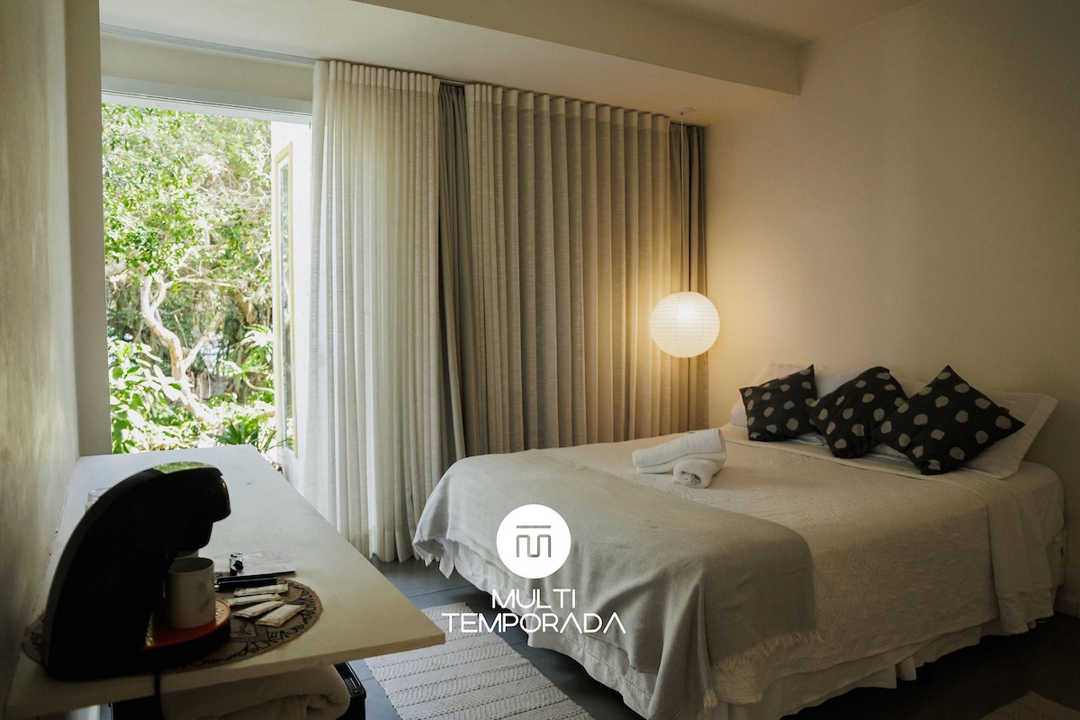 Une chambre d’hôtel avec un lit, des rideaux, un bureau avec une machine à café et une lampe.
