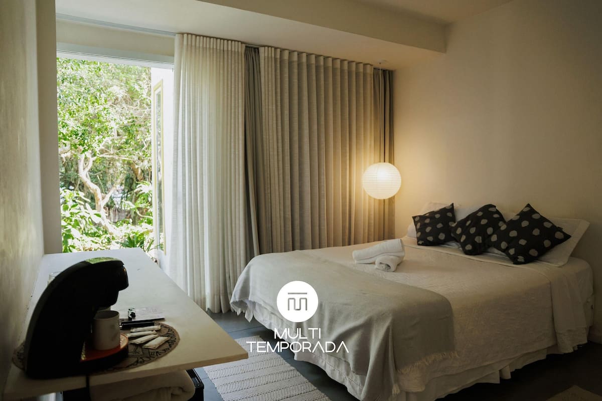 Una habitación de hotel con cama, cortinas, un escritorio y una cafetera, además de una lámpara.