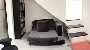 A modern living room with a grey sofa, a black bookshelf, and a staircase leading to an upper level. - Quinta da Margem (Florianópolis)