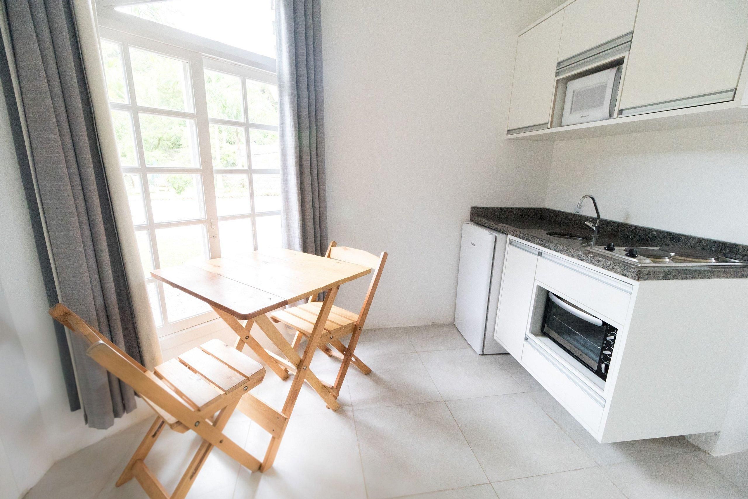 Una cocina con armarios blancos, horno empotrado, microondas y una ventana con cortinas.