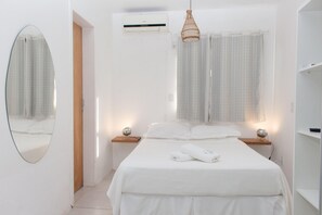 Un dormitorio con cama, mesitas de noche, un espejo, un equipo de aire acondicionado y una lámpara colgante.