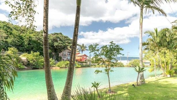 A tropical resort with a clear turquoise pool, lush greenery, and a view of the ocean. - Quinta da Margem (Florianópolis)