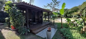 Un espacio al aire libre cubierto con terraza, rodeado de plantas en macetas y un jardín.