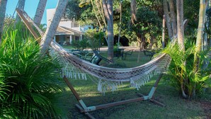 Una hamaca en un jardín exuberante con árboles y un edificio al fondo.
