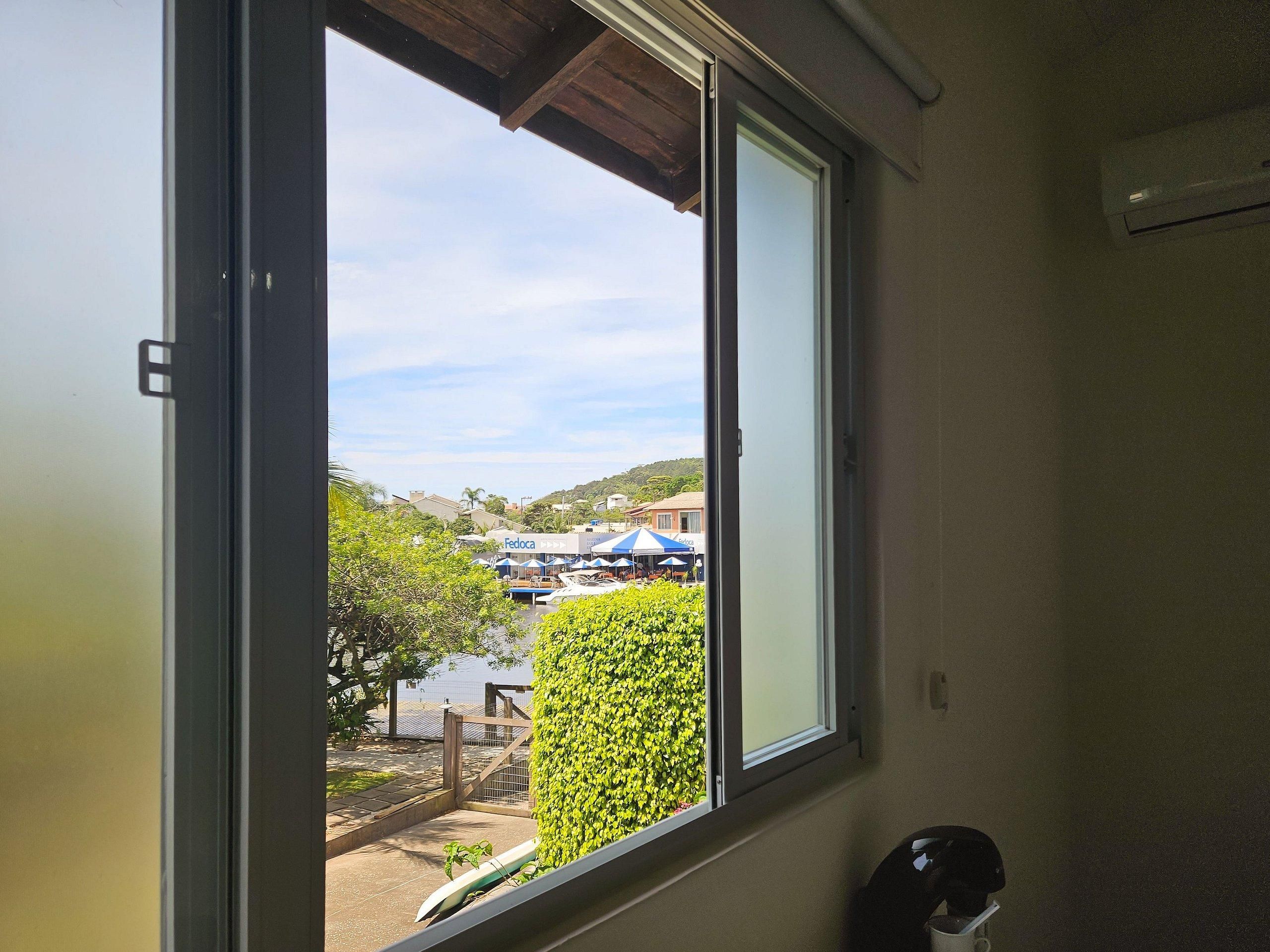 Una ventana con vista a un edificio con el letrero 'Fedoca', una cerca de madera y un seto bien cuidado.