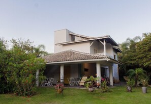 Una casa de dos pisos con techo de tejas, un porche cubierto y un jardín con macetas y mobiliario exterior.