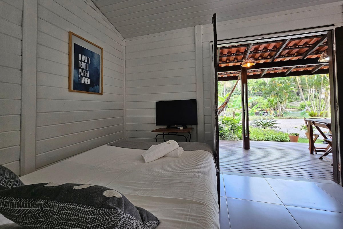 A bedroom with a bed, a television, and a view of a garden through an open door.