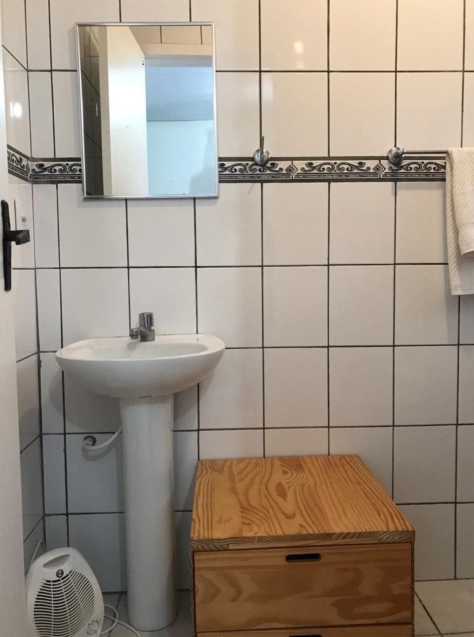 Une salle de bain avec un lavabo blanc, un miroir et une boîte en bois.
