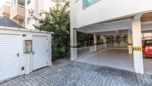 A covered parking area with a tiled floor and a white building with balconies. - 150m do Mar! Cobertura Duplex com Piscina Privada (Bombinhas)