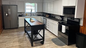 Une cuisine moderne avec des meubles blancs, des appareils en acier inoxydable et une table en bois.