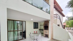 A two-story building with a patio area featuring a brick oven and a table with chairs. - Cohost Apt Praia 101a 80m do mar e 250m da Vila (Ipojuca)